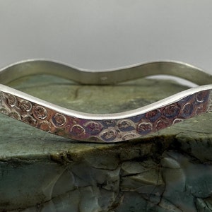 May include: A silver bangle bracelet with a wavy design and a hammered texture.