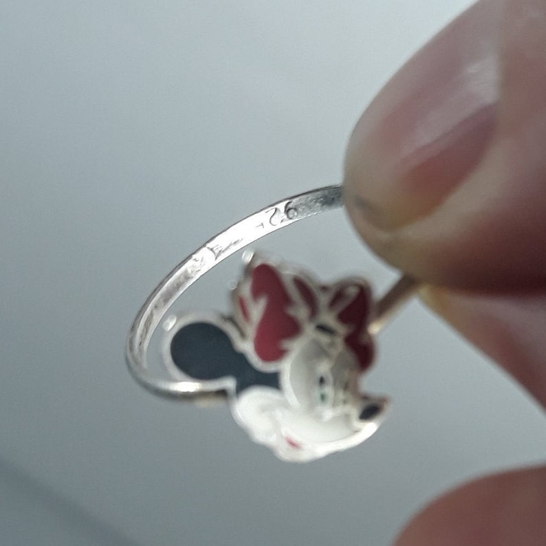 May include: Silver ring with a red and black enamel Minnie Mouse design. The ring is marked with the number "925" on the inside band.