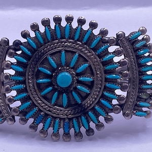 Puede incluir: Un brazalete de plata con piedras turquesa en forma de sol.
