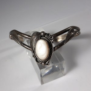 Puede incluir: Una pulsera de plata con una piedra ovalada blanca engastada en un diseño de hoja de plata.