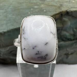 May include: A silver ring with a white, opaque gemstone. The gemstone has a rectangular shape and is set in a bezel setting. The ring is on a white background.