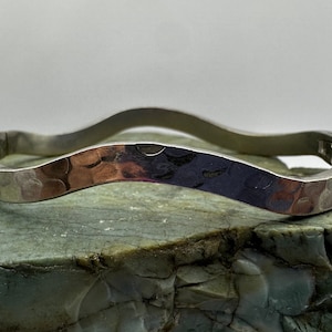May include: A silver hammered bangle bracelet with a wavy design.