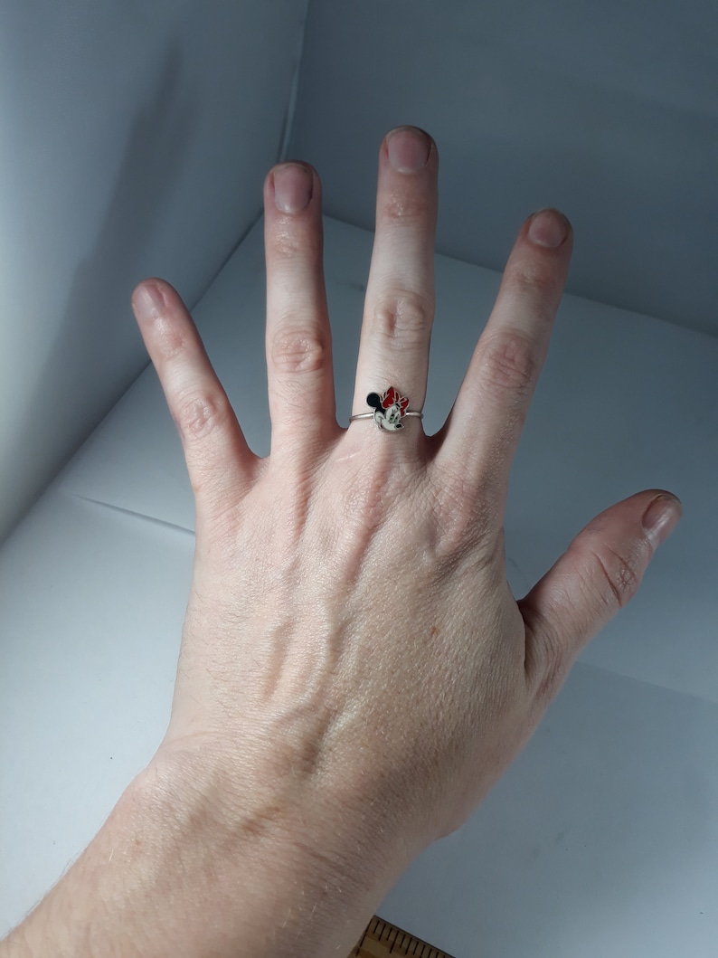 May include: A silver ring with a red and black Minnie Mouse design.