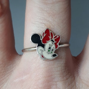May include: A silver ring with a red, white, and black enamel Minnie Mouse design.