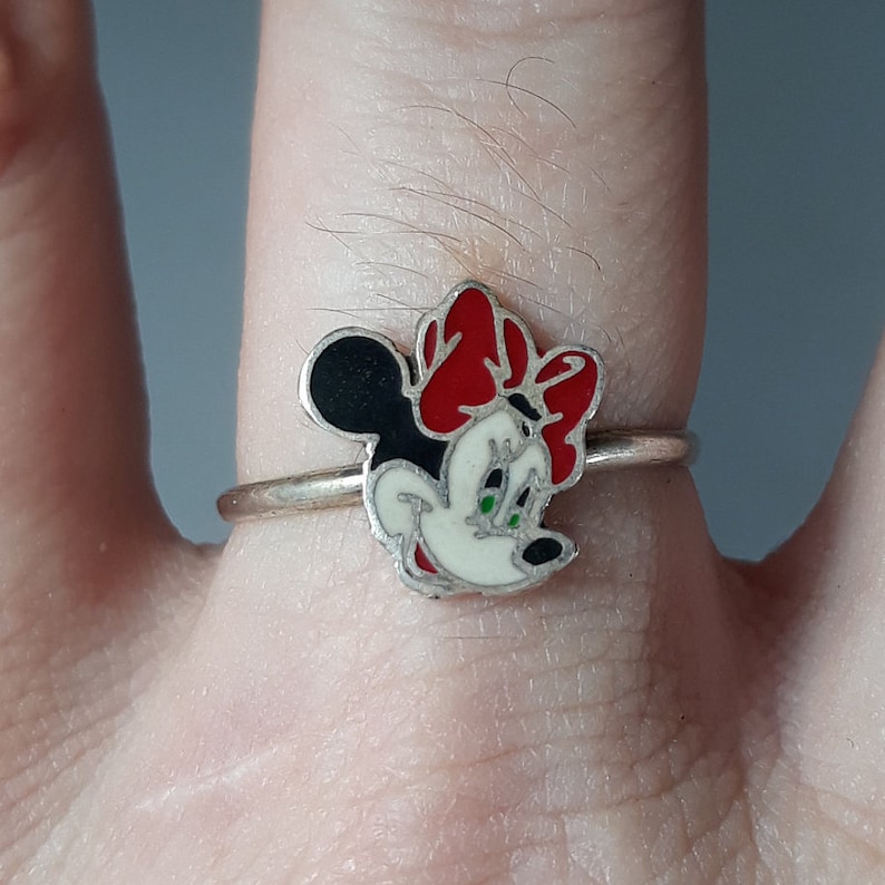 May include: A silver ring with a red, white, and black enamel Minnie Mouse design.