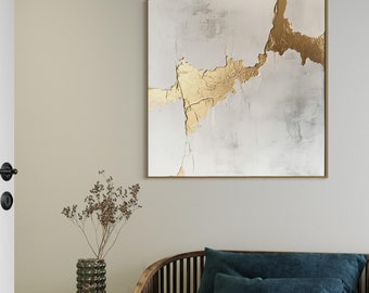 May include: A gold and white abstract painting with a wooden frame hangs on a white wall above a dark blue sofa with wooden slats. A vase with dried flowers sits on a small wooden table.