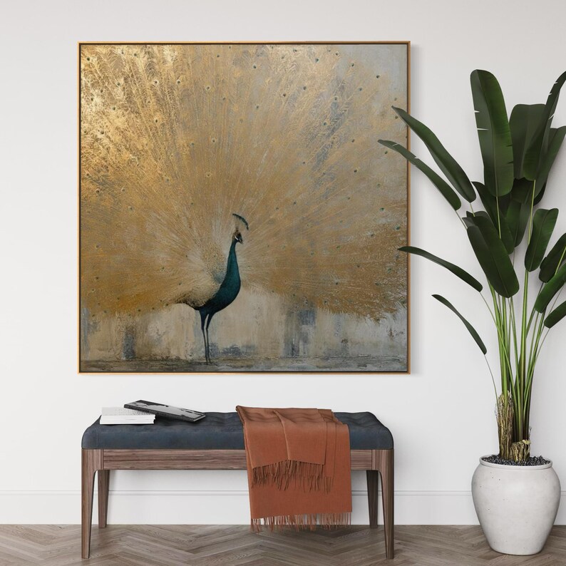 Op de afbeelding: Een vierkant wandkunstwerk met een pauw met een grote, uitgewaaierde staart in metallic bladgoud. Het lichaam van de pauw is diep blauwgroen en staat tegen een getextureerde achtergrond in neutrale tinten. Het kunstwerk heeft een dunne gouden rand.