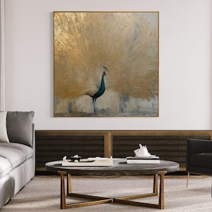 Op de afbeelding: Een vierkant wandkunstwerk met een pauw met een grote, uitgewaaierde staart in tinten van metallic goud en gedempt grijs. De vogel is in profiel afgebeeld tegen een gestructureerde, neutrale achtergrond, omlijst door een dunne, goudkleurige rand.
