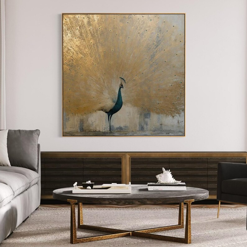 Op de afbeelding: Een vierkant wandkunstwerk met een pauw met een grote, uitgewaaierde staart in tinten van metallic goud en gedempt grijs. De vogel is in profiel afgebeeld tegen een gestructureerde, neutrale achtergrond, omlijst door een dunne, goudkleurige rand.