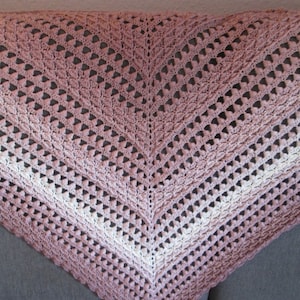 Może przedstawiać: Ręcznie robiony szal w kolorze różowym i białym. Szal wykonany jest delikatnym ściegiem i ma trójkątny kształt.