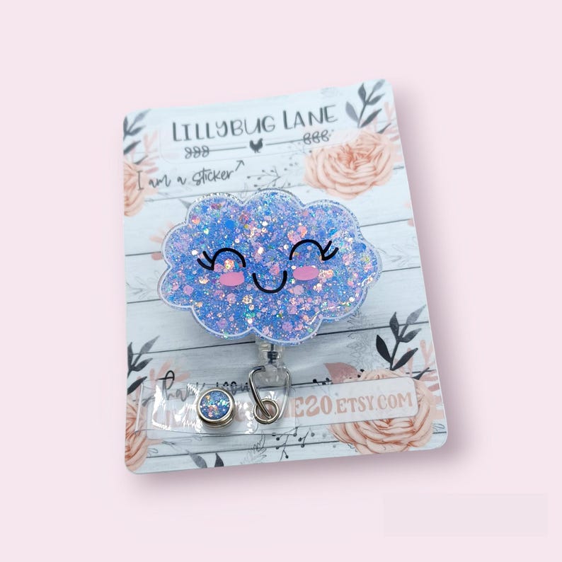 K&ouml;nnte beinhalten: Eine blaue Glitzerwolke mit einem l&auml;chelnden Gesicht auf wei&szlig;em Hintergrund. Die Wolke ist an einem einziehbaren Ausweishalter mit einem silbernen Clip befestigt. Der Text "Lillybug Lane" ist auf der Karte sichtbar.