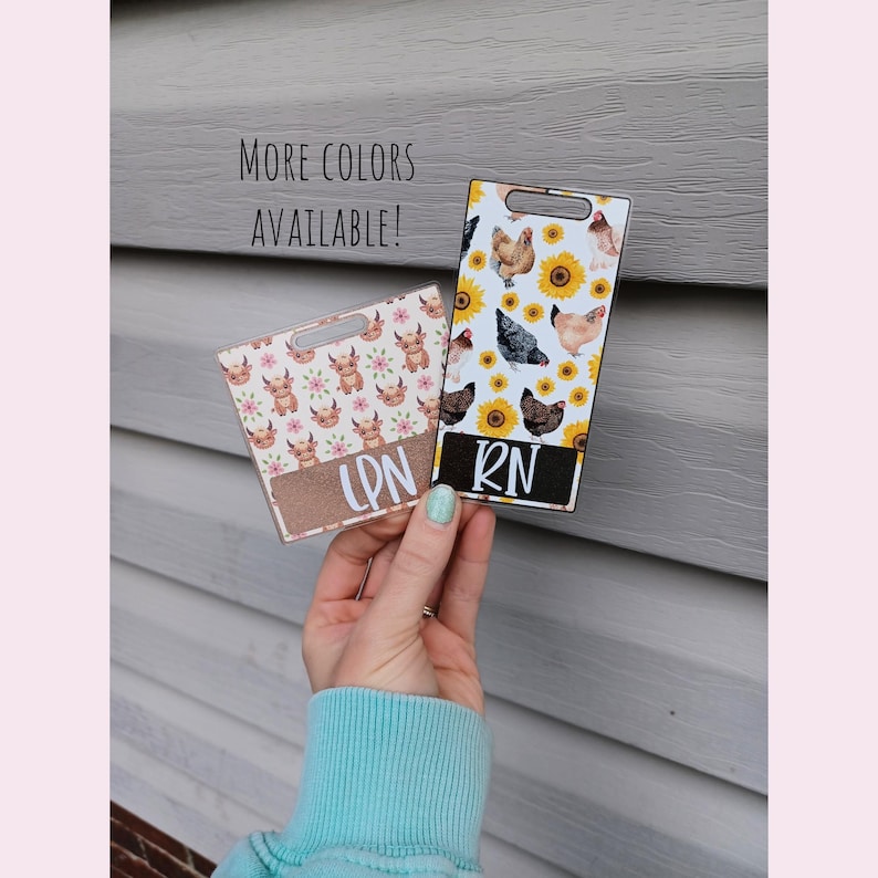 May include: Two plastic badge holders with a sunflower and chicken design. One holder says "RN" and the other says "LPN".