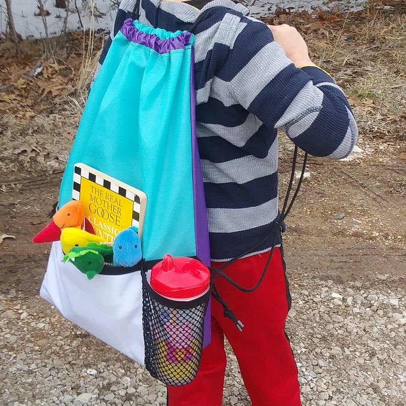 May include: A turquoise, purple, and white drawstring backpack with a mesh side pocket. The backpack is filled with a book, "The Real Mother Goose", and several stuffed toys. A red cup is in the mesh pocket.