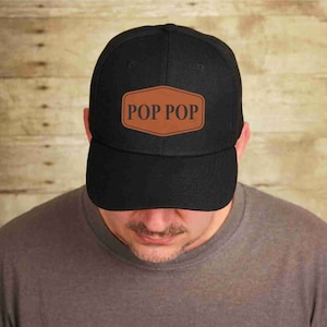 May include: Black baseball cap with a brown leather patch that says "POP POP" in white text.