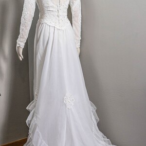 May include: A white wedding dress with long sleeves and a lace bodice. The dress has a full skirt with ruffles and a long train.