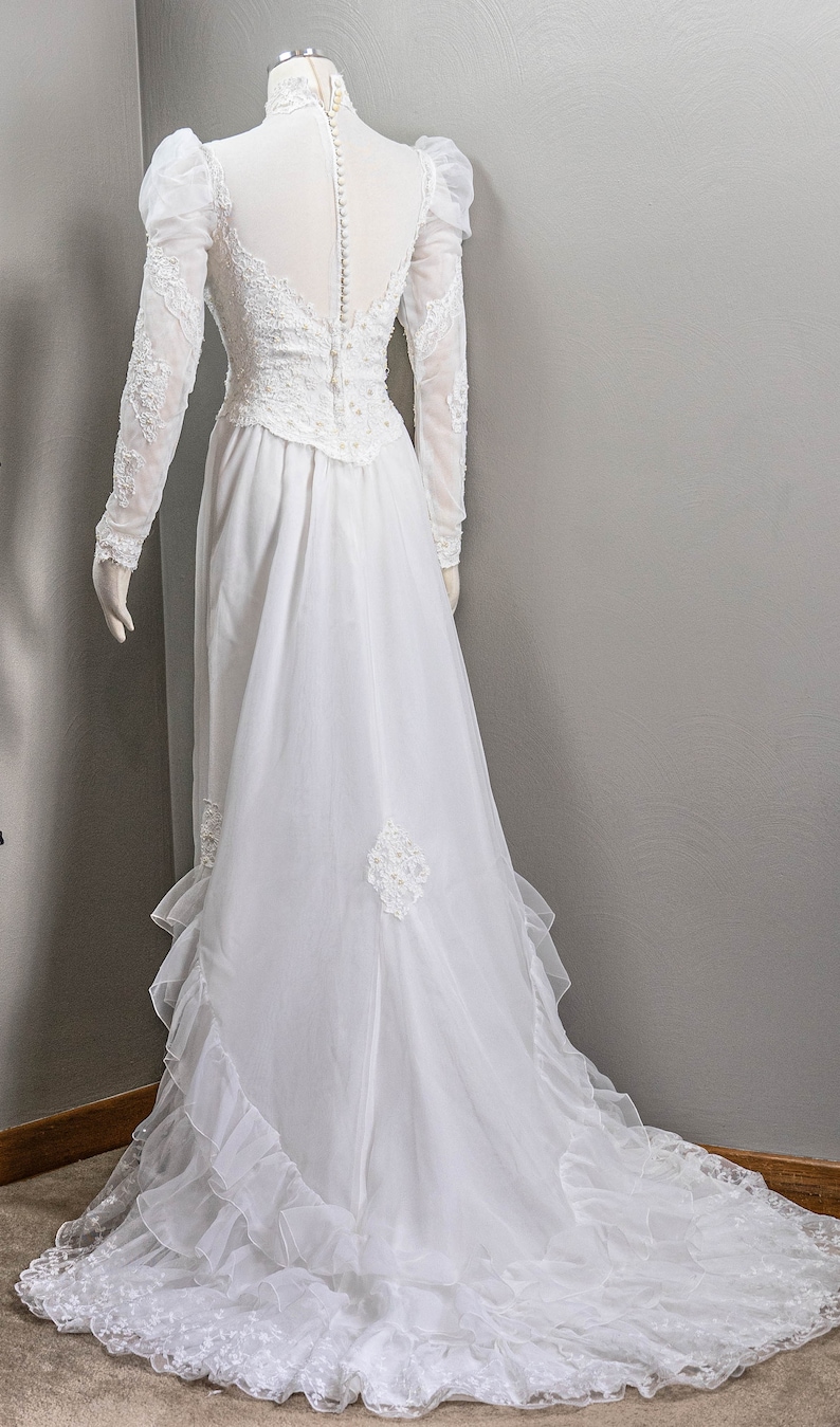 May include: A white wedding dress with long sleeves and a lace bodice. The dress has a full skirt with ruffles and a long train.