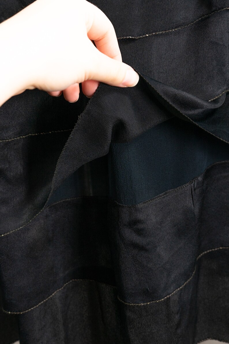May include: Black skirt with a layered design. The skirt is made of a sheer fabric with a solid black lining. The layers are separated by thin gold stitching.