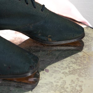 May include: A pair of dark green canvas shoes with laces. The shoes have a worn look and are sitting on a textured surface.