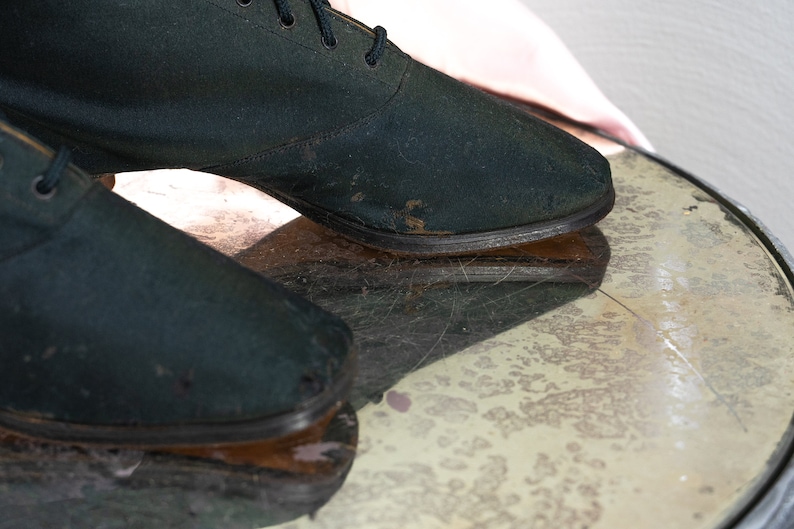 May include: A pair of dark green canvas shoes with laces. The shoes have a worn look and are sitting on a textured surface.