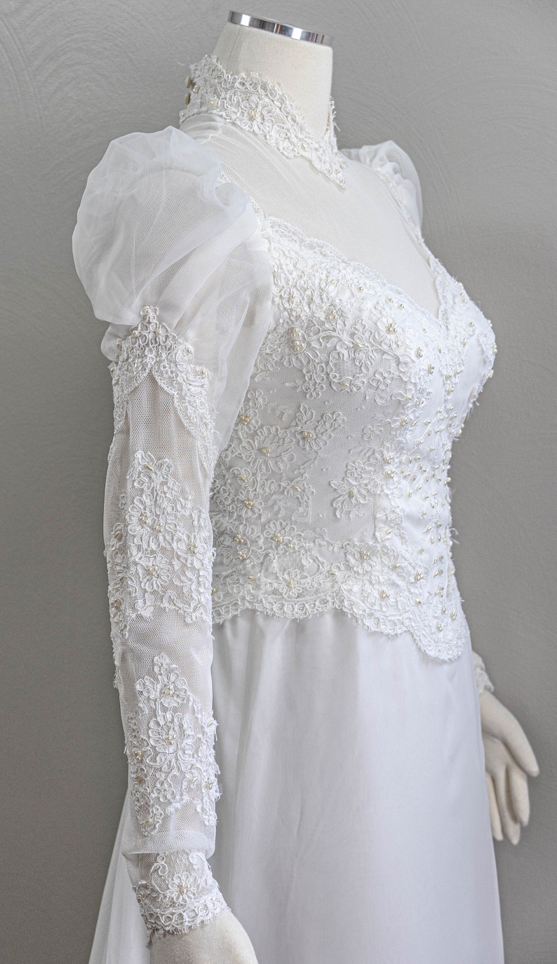 May include: A white wedding dress with long sleeves and a high neckline. The dress is made of lace and tulle and features a fitted bodice and a flowing skirt.