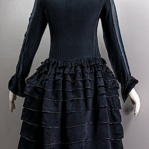 May include: A black dress with a ruffled skirt and sheer sleeves. The dress has a lace trim at the neckline and gold trim on the ruffles.