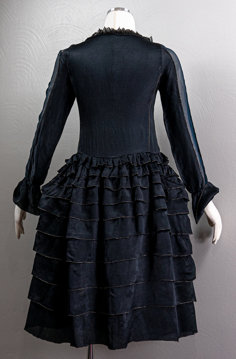 May include: A black dress with a ruffled skirt and sheer sleeves. The dress has a lace trim at the neckline and gold trim on the ruffles.