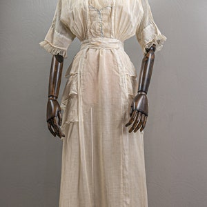 May include: A white sheer dress with a ruffled skirt and a fitted bodice. The dress has a simple design and is made of a lightweight fabric.