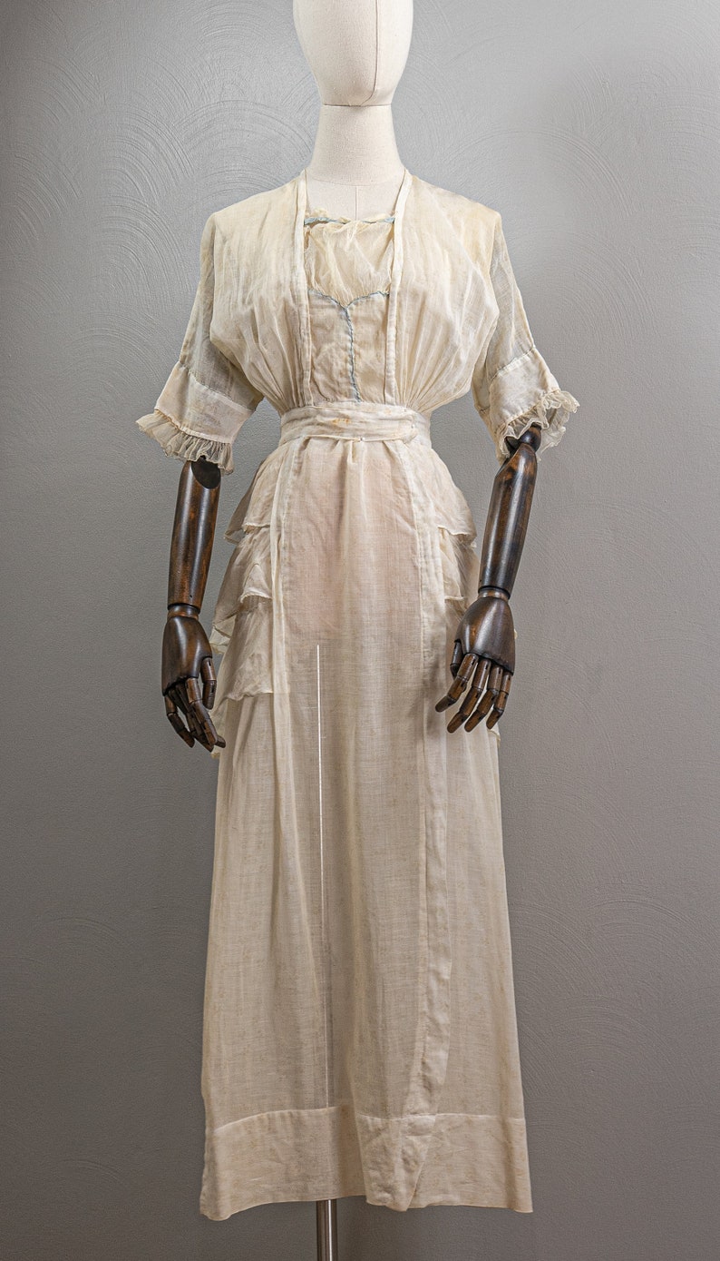 May include: A white sheer dress with a ruffled skirt and a fitted bodice. The dress has a simple design and is made of a lightweight fabric.