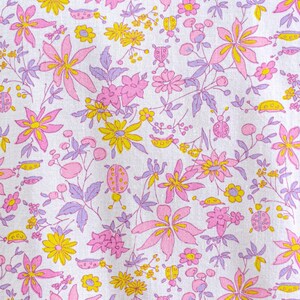 Puede incluir: Una tela blanca con un estampado floral repetitivo. El dise&ntilde;o presenta flores rosas, amarillas y moradas, junto con peque&ntilde;as ilustraciones de mariquitas. Las flores var&iacute;an en tama&ntilde;o y forma, creando una impresi&oacute;n caprichosa y colorida.