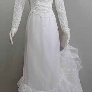 May include: A white wedding dress with a high neckline, long sleeves, and a lace bodice. The skirt is made of layers of tulle and has a ruffled hem.