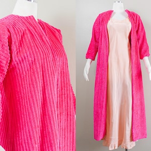 May include: A vibrant pink, ribbed-textured robe with three-quarter sleeves. The robe is open, revealing a peach-colored slip dress underneath. The ensemble is displayed on a mannequin, showcasing the vintage style of the clothing.