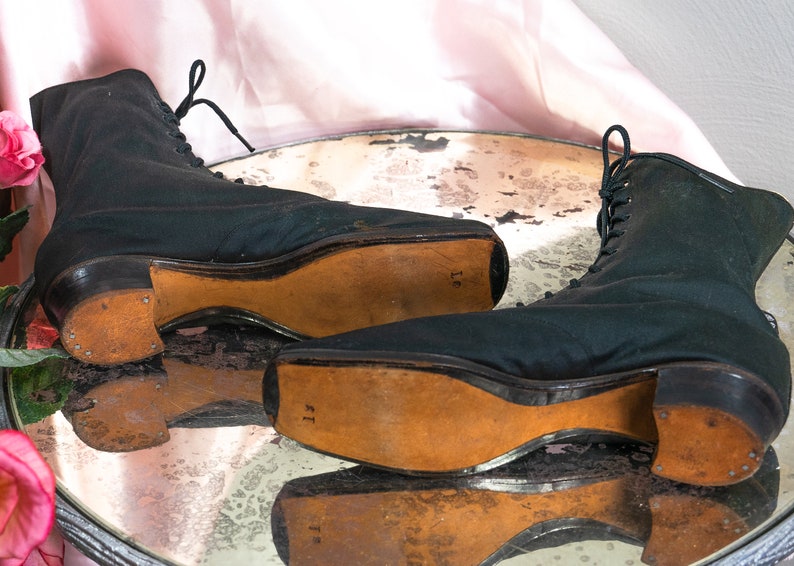 May include: A pair of black lace-up boots with leather soles. The boots have a rounded toe and a low heel. The soles are marked with the size "11" and "16".