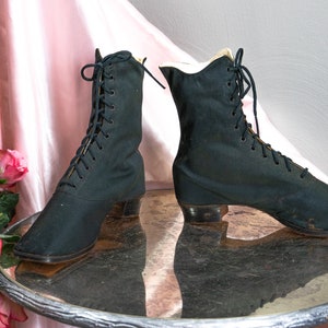 May include: A pair of black lace-up boots with a low heel. The boots are made of a soft, fabric material and have a pointed toe.