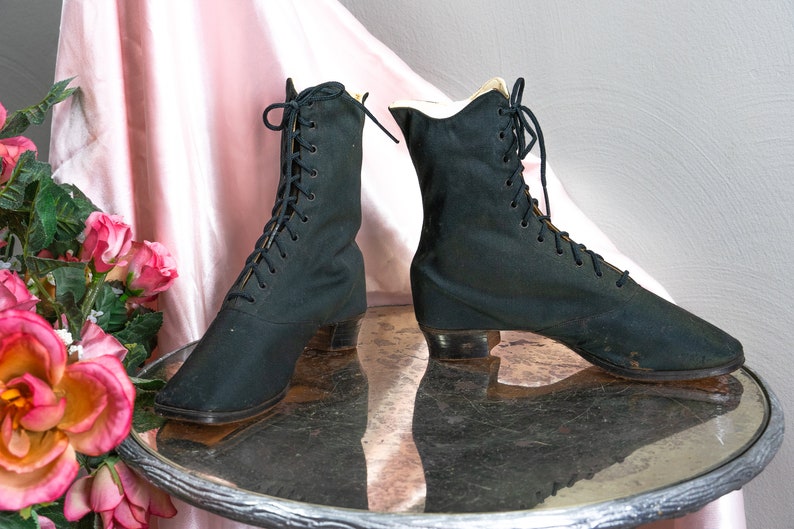 May include: A pair of black lace-up boots with a low heel. The boots are made of a soft, fabric material and have a pointed toe.