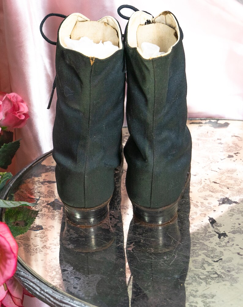 May include: A pair of black lace-up boots with a white lining. The boots are sitting on a mirrored surface.