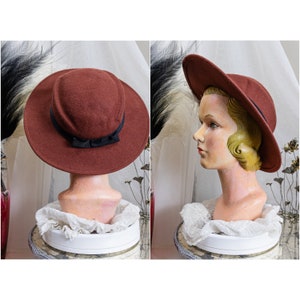 May include: A brown felt hat with a black ribbon and bow. The hat is sitting on a white stand.