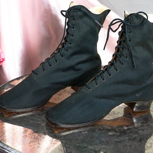 May include: A pair of black lace-up boots with a low heel. The boots are made of a canvas-like material and have a pointed toe.