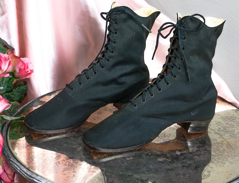 May include: A pair of black lace-up boots with a low heel. The boots are made of a canvas-like material and have a pointed toe.