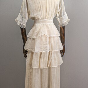 May include: A white, tiered, cotton dress with a fitted bodice and a full skirt. The dress has a V-neckline and short sleeves with lace trim.