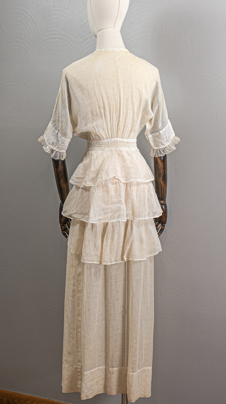 May include: A white, tiered, cotton dress with a fitted bodice and a full skirt. The dress has a V-neckline and short sleeves with lace trim.