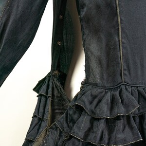 May include: A black dress with a ruffled hem and a gold trim. The dress has a long sleeve and a button closure on the side.