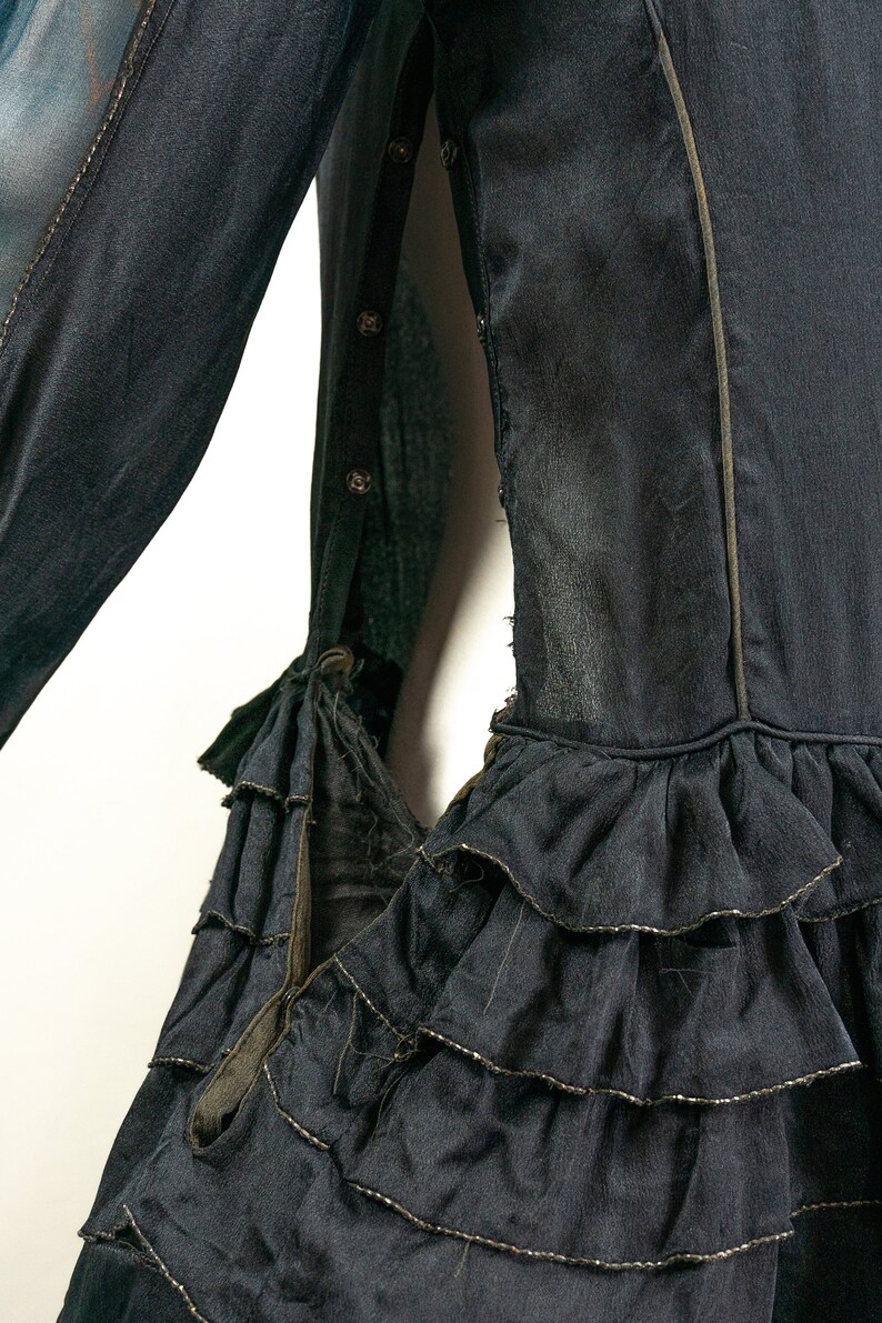 May include: A black dress with a ruffled hem and a gold trim. The dress has a long sleeve and a button closure on the side.