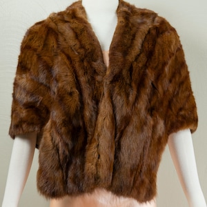 Puede incluir: Bolero de piel marrón con mangas cortas. La chaqueta se exhibe en un maniquí. La piel parece suave y tiene un color marrón oscuro intenso. El bolero tiene un diseño de cuello en V.