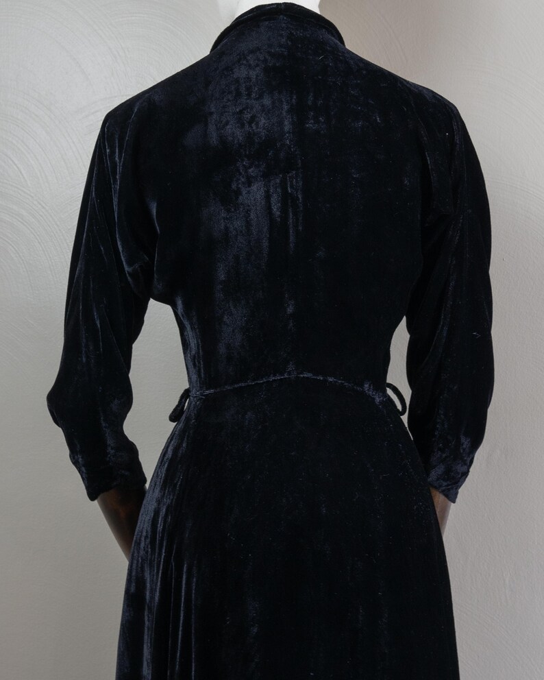 K&ouml;nnte beinhalten: Ein schwarzes Samtkleid mit langem Rock und langen &Auml;rmeln. Das Kleid hat einen Wickelstil und wird in der Taille gebunden.