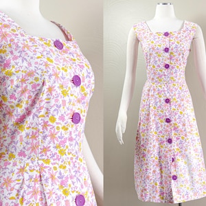 Puede incluir: Vestido sin mangas con estampado floral, cuello cuadrado y una fila de botones morados. El vestido presenta un fondo blanco con estampados florales rosas, amarillos y morados. El vestido se exhibe en un maniqu&iacute;.