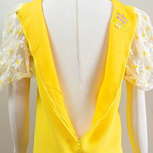 May include: A bright yellow dress with a zipper down the back. The dress features sheer, puffy sleeves adorned with white daisy appliqu&eacute;s. A tag on the dress reads "a. stopper design California".