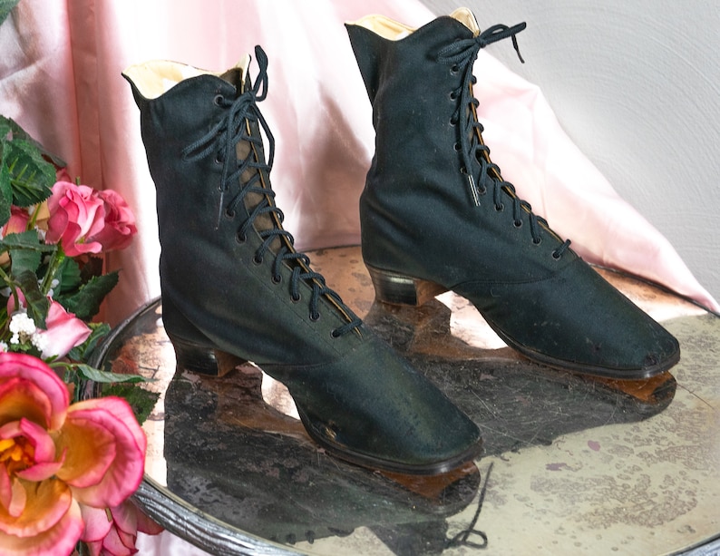 May include: Two black lace-up ankle boots with low heels. The boots are made of a smooth fabric and have a pointed toe.