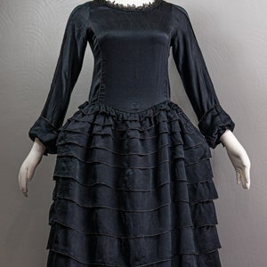 May include: A black satin dress with a ruffled skirt and long sleeves. The dress has a lace neckline and is on a mannequin.
