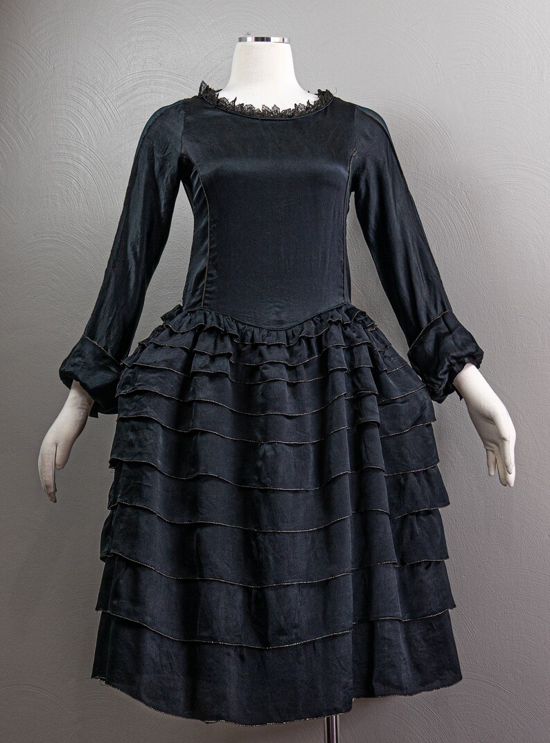 May include: A black satin dress with a ruffled skirt and long sleeves. The dress has a lace neckline and is on a mannequin.
