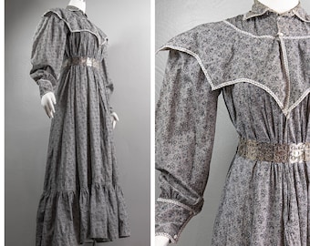 May include: A long, grey, floral print dress with a white lace collar and cuffs. The dress has a cinched waist with a silver belt and a tiered skirt.